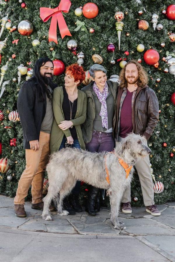 friends and their dog by a large christmas tree